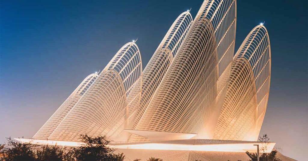 Modern Abu Dhabi museum with illuminated futuristic architecture and sweeping curved structures against an evening sky.